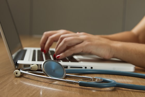 Stethoscope resting on a wooden desk beside a laptop used for reviewing lab results