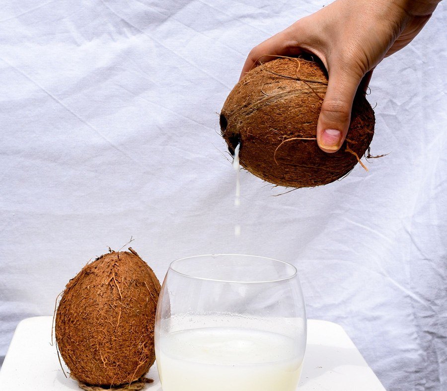 Fresh coconut water being poured into a glass on a light background