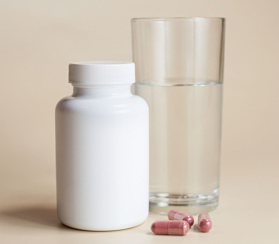 White supplement bottle with capsules beside a glass of water