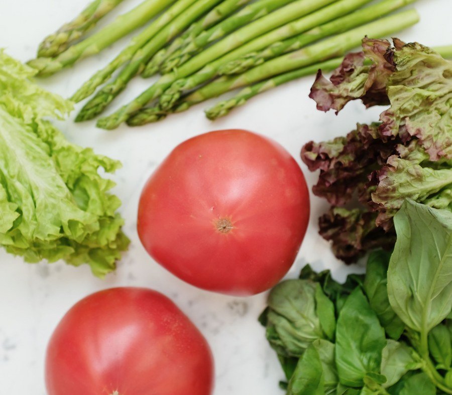 Top-down view of fresh asparagus, lettuce, basil and tomatoes on a light surface