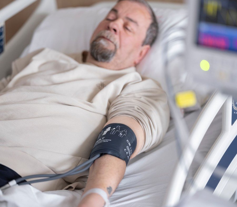 Older man resting in a hospital bed with a blood pressure monitor attached